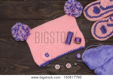 Knitted baby cap and Slippers, yarn for knitting on wooden table. The view from the top. Sewing accessories.