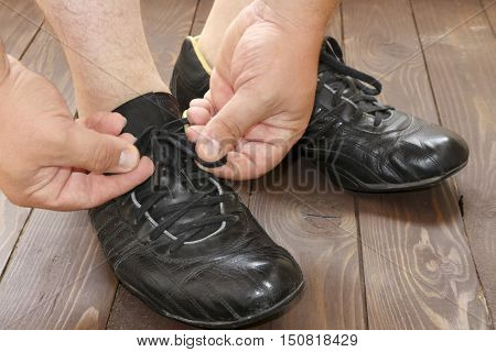 Tying Shoe laces a man sits on a wooden floor. the view from the top. Dark shoes on wooden background.