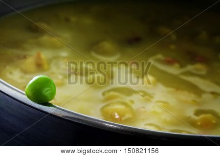 Fresh green pea on the edge of a pot full with overcooked vegetable soup concept for cooking vitamin-preserving or metaphor for a dangerous dare close up with elected focus narrow depth of field
