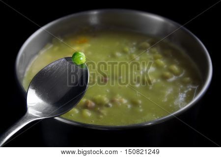 Fresh green pea on a spoon over a pot with dead-boiled soup Kitchen drama concept of vitamins damning cooking or metaphor for a dangerous dare close up with selected focus and narrow depth of field