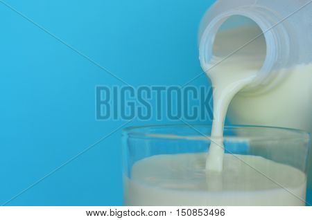 Plastic milk bottle pouring milk into a glass over a blue background