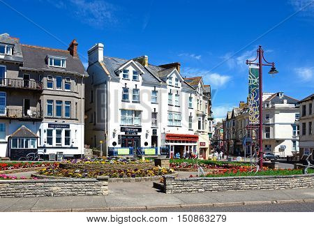 SEATON, UNITED KINGDOM - JULY 18, 2016 - Pretty flowerbeds on a traffic island with town centre buildings and shops to the rear Seaton Devon England UK Western Europe, July 18, 2016.