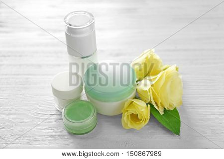Cosmetic bottles and eustoma flowers on light wooden background