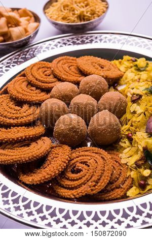 Plate full of indian festival food or diwali food or snacks like laddu, chivda, chakali or murukku, sev and shankar pale, sweet and salty snack food
