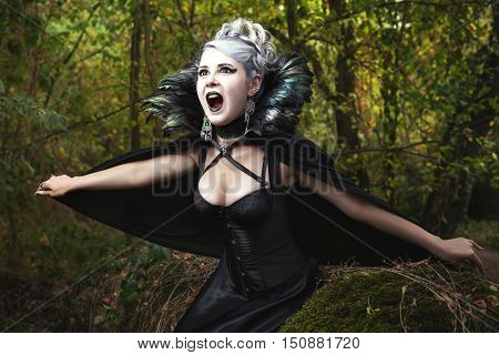 Scary girl screams she in gothic black dress in the forest.