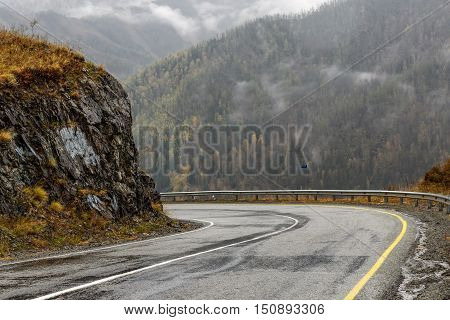 Scenic view of the hairpin bend wet winding road through the pass part of the mountain serpentine in autumn cloudy weather with fog