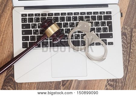 Handcuffs and gavel on laptop on wooden background