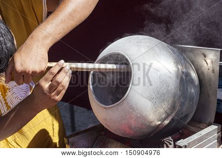 Man preparing sunflower seeds coated in caramel with long wooden spoon in a rotatory pot