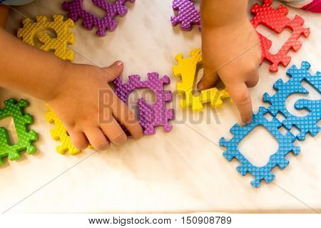 Colorful foam puzzle letters and numbers in kid's hands on a light table. Baby puts puzzle of letters and numbers. Close-up