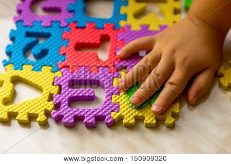 Colorful foam puzzle letters and numbers in kid's hands on a light table. Baby puts puzzle of letters and numbers. Close-up
