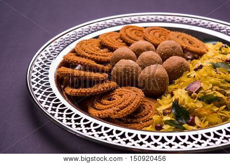 Plate full of indian festival food or diwali food or snacks like laddu, chivda, chakali or murukku, sev and shankar pale, sweet and salty snack food
