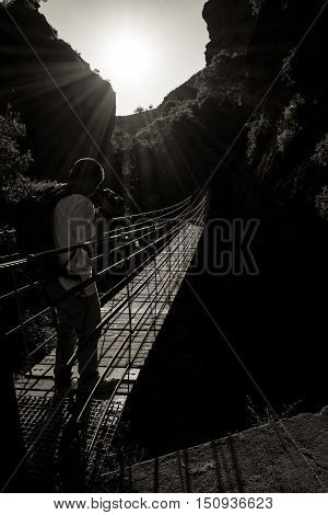 Hanging bridge over a deep and dark canyon against the sun