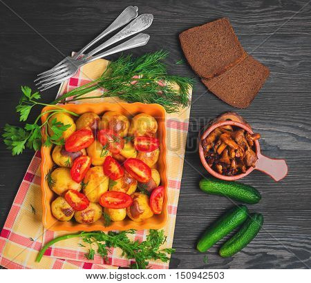 Autumn dinner Baked roasted young potatoes tomatoes in ceramic form. Greens for baked roasted potatoes thyme parsley dill. Roasted with potatoes Chanterelle Mushrooms dark wooden background. Top view