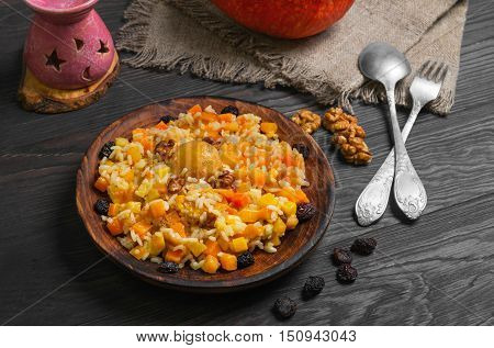 Pumpkin risotto with raisins. Rice porridge with sweet pumpkin raisins nuts apricot. Fresh pumpkin for Halloween rice. Sacking dark wood background.