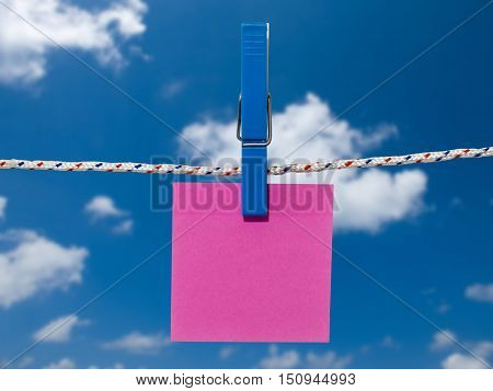 Single blank square of red paper suspended from a washing line by plastic peg against blue sky.