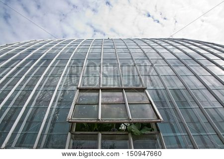 STOCKHOLM SWEDEN - MAY 13 2014: Bergianska garden and Victoria building glass greenhouse cupola and open window with plant sticking out on a cloudy day on May 13 2014 in Stockholm Sweden.