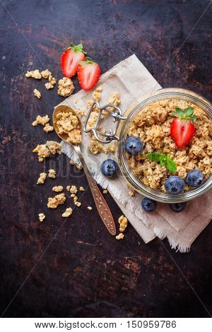 Breakfast, healthy food concept. Homemade muesli granola with berries in a jar on rusty black table. Selective focus, copy space background, top view flat lay overhead