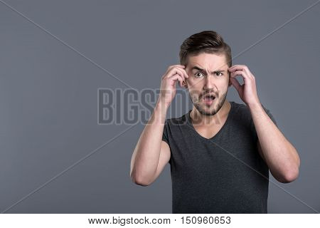 Huge shock. Shocked bearded young man opening his mouth and raising his hands while standing isolated in grey background