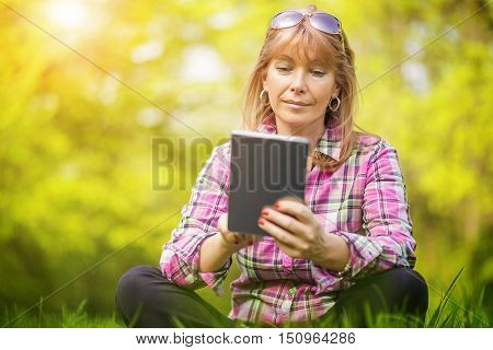 Beautiful mature woman in the park using a digital tablet.