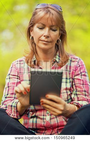 Relaxing in nature.Beautiful mature woman in the park using a digital tablet.