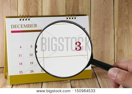 Magnifying glass in hand on calendar you can look third date of monthFocus number three in DecemberConcept in business and meetings.