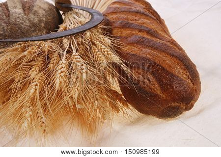 bunch of mown wheat ears with vintage handmade reaper hook sickle and rye and white dark french fresh bread loaf on light linen tablecloth