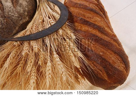 bunch of mown wheat ears with vintage handmade reaper hook sickle and rye and white dark french fresh bread loaf on light linen tablecloth