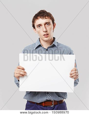 sad guy with a sheet of white paper in hands. young man holding a blank sheet of white paper for your text. looking at camera. mock-up. isolated on grey background