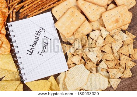 Inscription Unhealthy Food In Notebook And Heap Of Crisps And Cookies