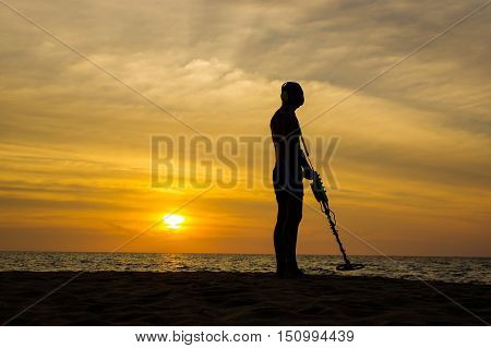 a treasure hunter with Metal detector on sunset on the beach