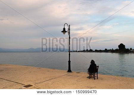 Old woman sitting lonely looking at the sunset against a dramatic sky.