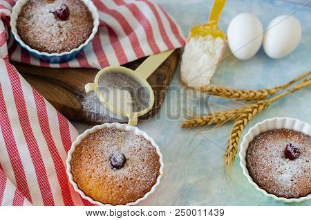 Cakes With Cerries On A Table In Small Porcelain Cups .there Are  Eggs, Flour, Wheat, Powdered Sugar