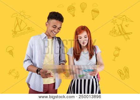 Tour Itinerary. Cheerful Young Friends Smiling And Looking Attentively At The Colorful Map Of The Wo