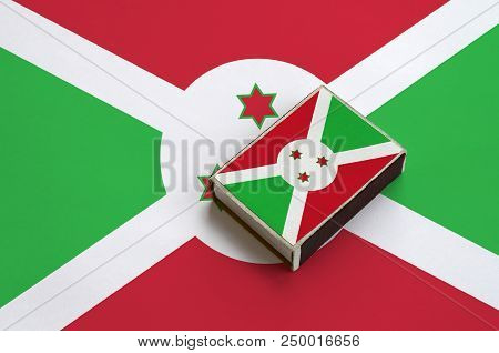 Burundi Flag  Is Pictured On A Matchbox That Lies On A Large Flag.