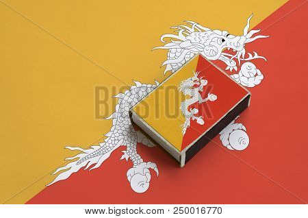 Bhutan Flag  Is Pictured On A Matchbox That Lies On A Large Flag.