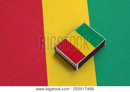 Guinea Flag  Is Pictured On A Matchbox That Lies On A Large Flag.