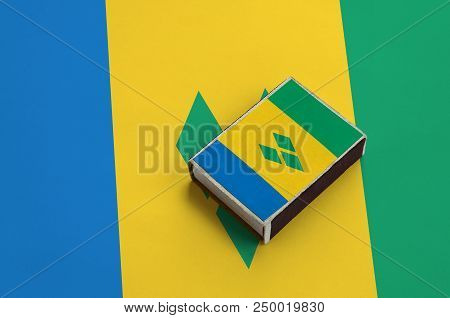 Saint Vincent And The Grenadines Flag  Is Pictured On A Matchbox That Lies On A Large Flag.