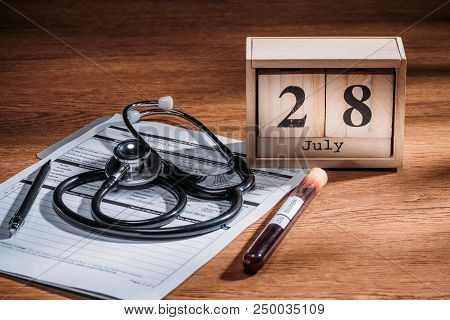 Selective Focus Of Test Flask With Blood Sample, Stethoscope, Medical Questionary And Wooden Calenda