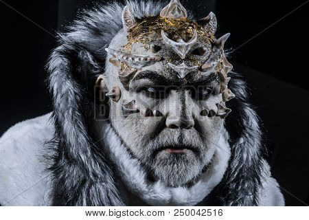 Demon With Horns On Head And Shinning Golden Skin Wearing White Fur Coat Isolated On Black Backgroun