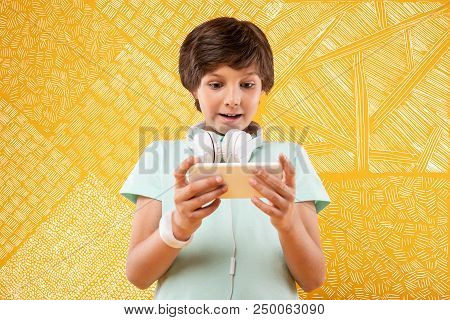 Feeling Impressed. Emotional Progressive Kid Feeling Impressed While Standing With A Modern Device I