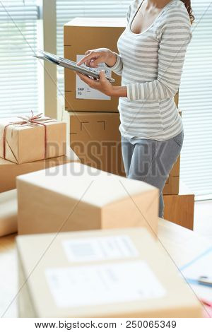 Woman Using Tablet Computer To Control Ammount Of Boxes She Needs To Ship