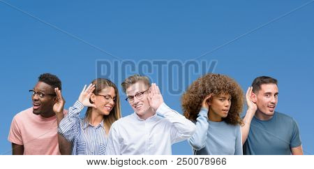 Composition of group of friends over blue blackground smiling with hand over ear listening an hearing to rumor or gossip. Deafness concept.