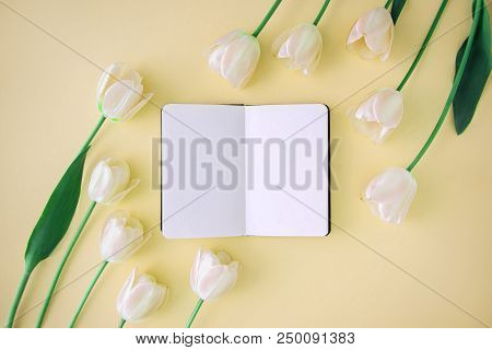 Opened Noteboog Around Beautiful Flowers. Yellow Background. Flat Lay Style.
