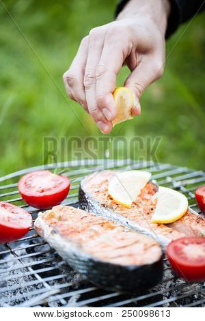 Salmon Preparation Process On Wooden Grill And Man Squezing Lemon Juicy. Grilled Fish Steaks On Fire