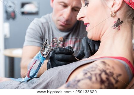 Side view close-up of a trendy woman smiling while getting a painless new tattoo in the modern studio of a skilled artist 