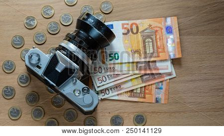 Euro Banknotes, Coins And A Camera On A Light Wooden Background.