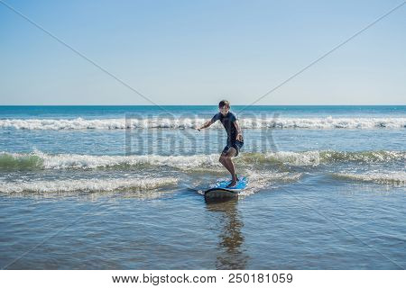 Young Man, Beginner Surfer Learns To Surf On A Sea Foam On The Bali Island.