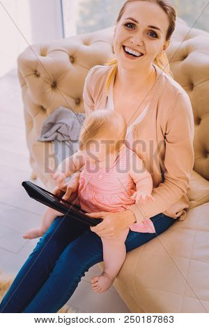 Smiling Baby Sitter. Positive Qualified Babysitter Smiling While Holding A Baby Involved In Using Mo