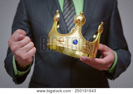 Businessman King Holding In Hands A Gold Crown And Showing A Fig Gesture. Refusal To Give First Plac
