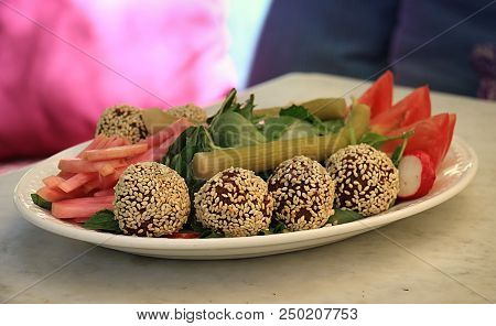 Falafel Balls Covered In Sesame In A Platter Along With The Traditional Accompanying Vegetables.